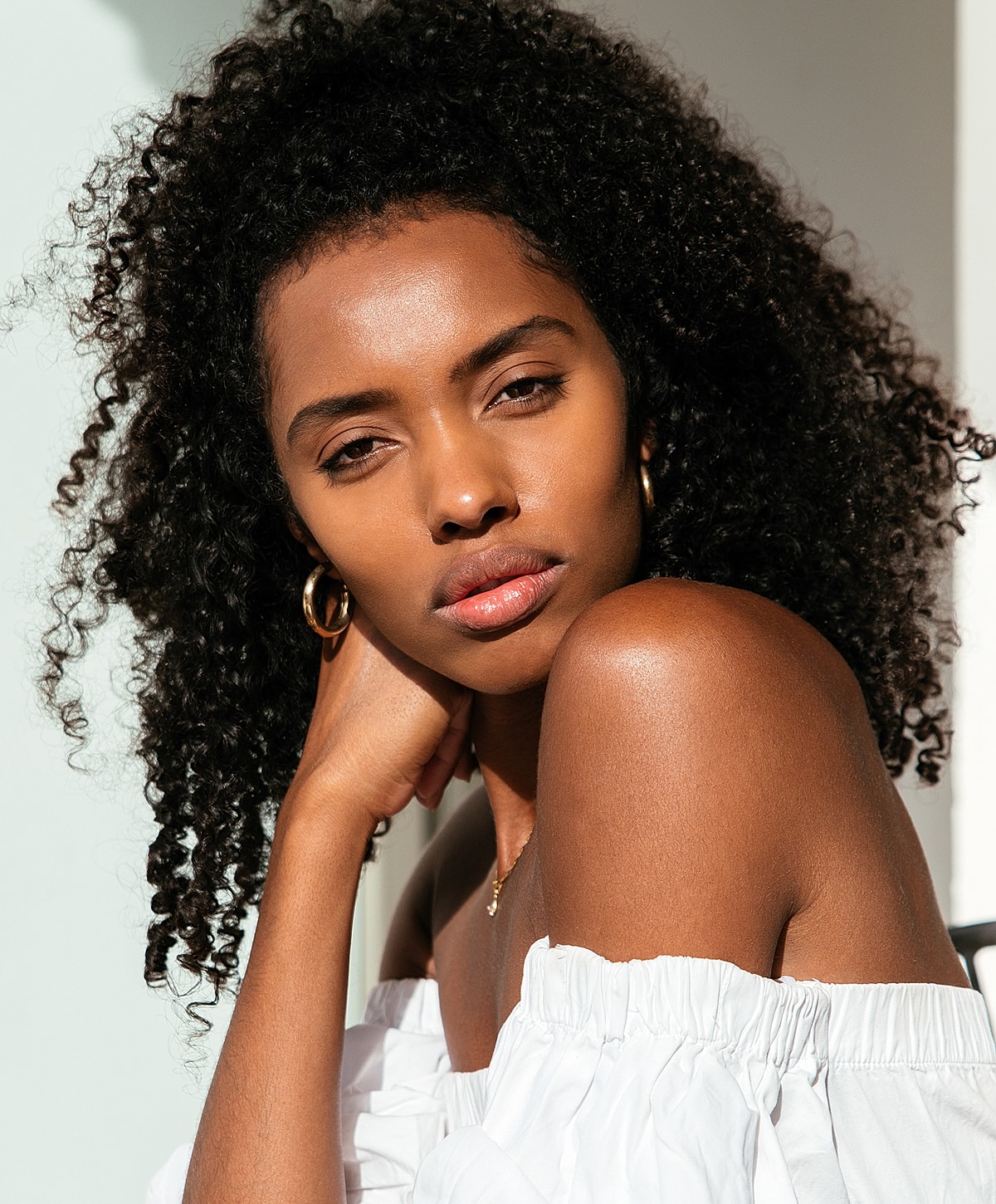 Woman with curly hair in white off-shoulder top.