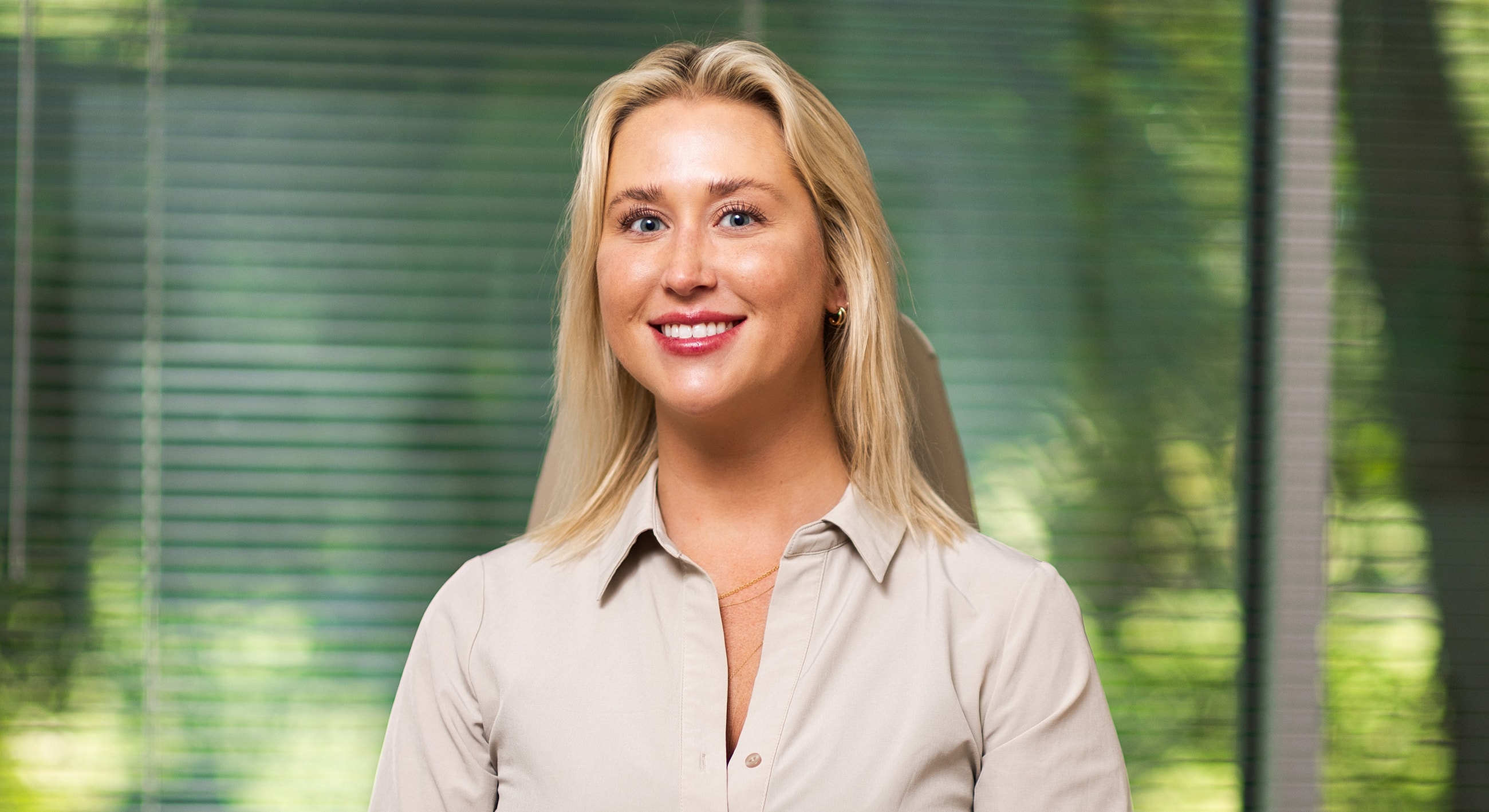 Smiling woman in professional setting with greenery.