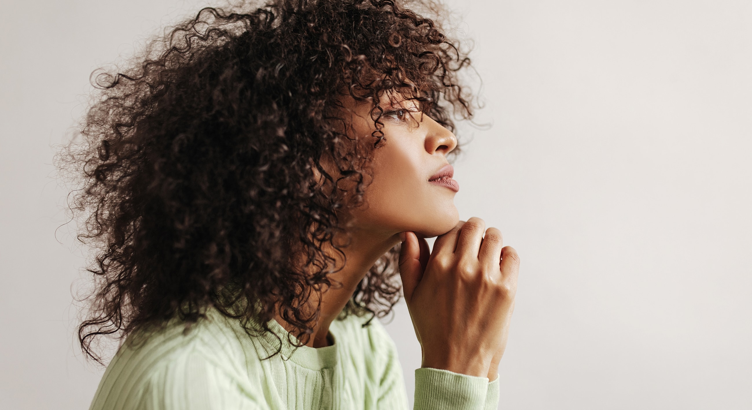 Woman with curly hair in thoughtful pose.